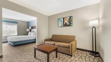 A hotel room with a bed, a sofa, a coffee table, a lamp, and a painting on the wall.