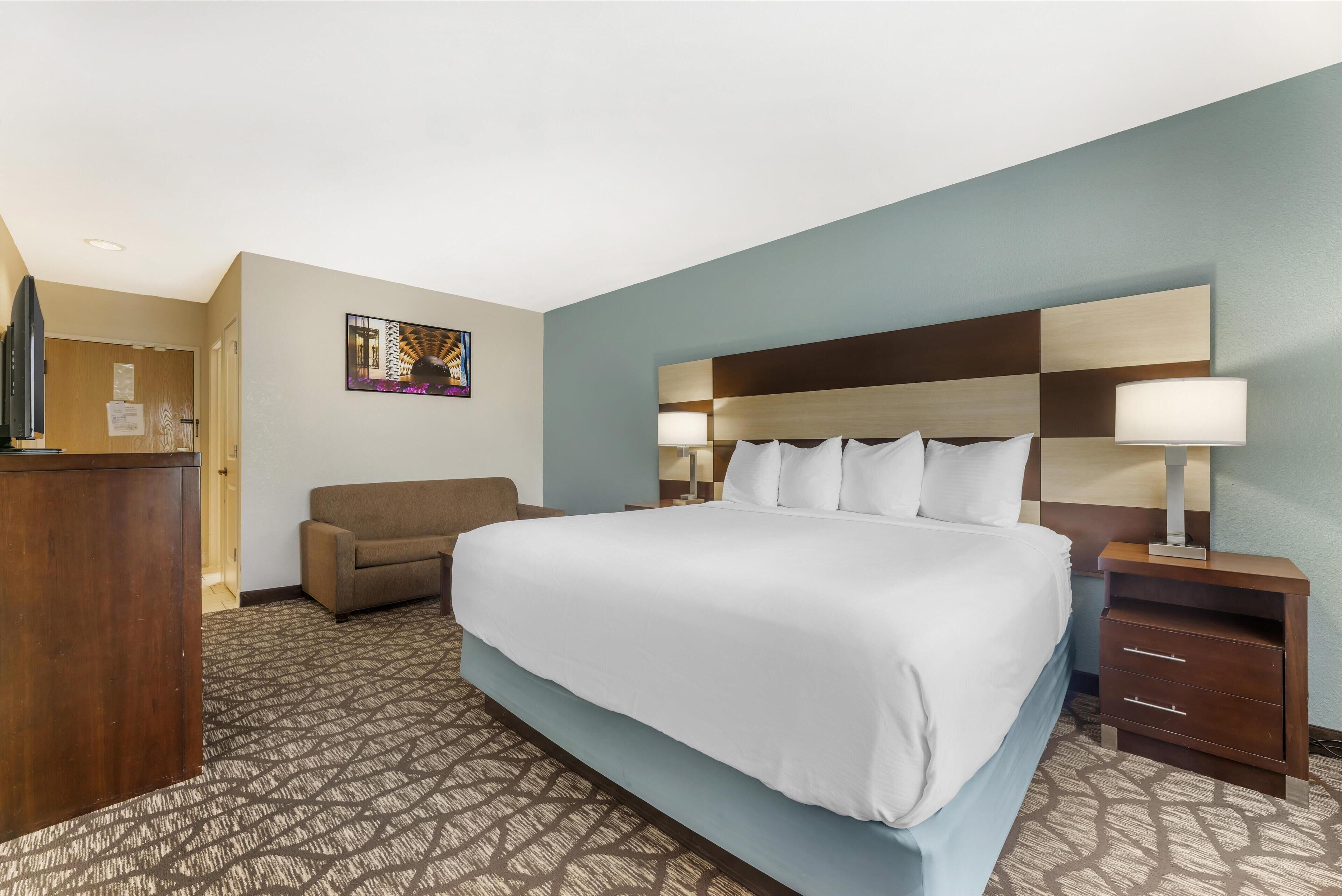A hotel room with a large bed, a desk, a couch, and a wall-mounted artwork.