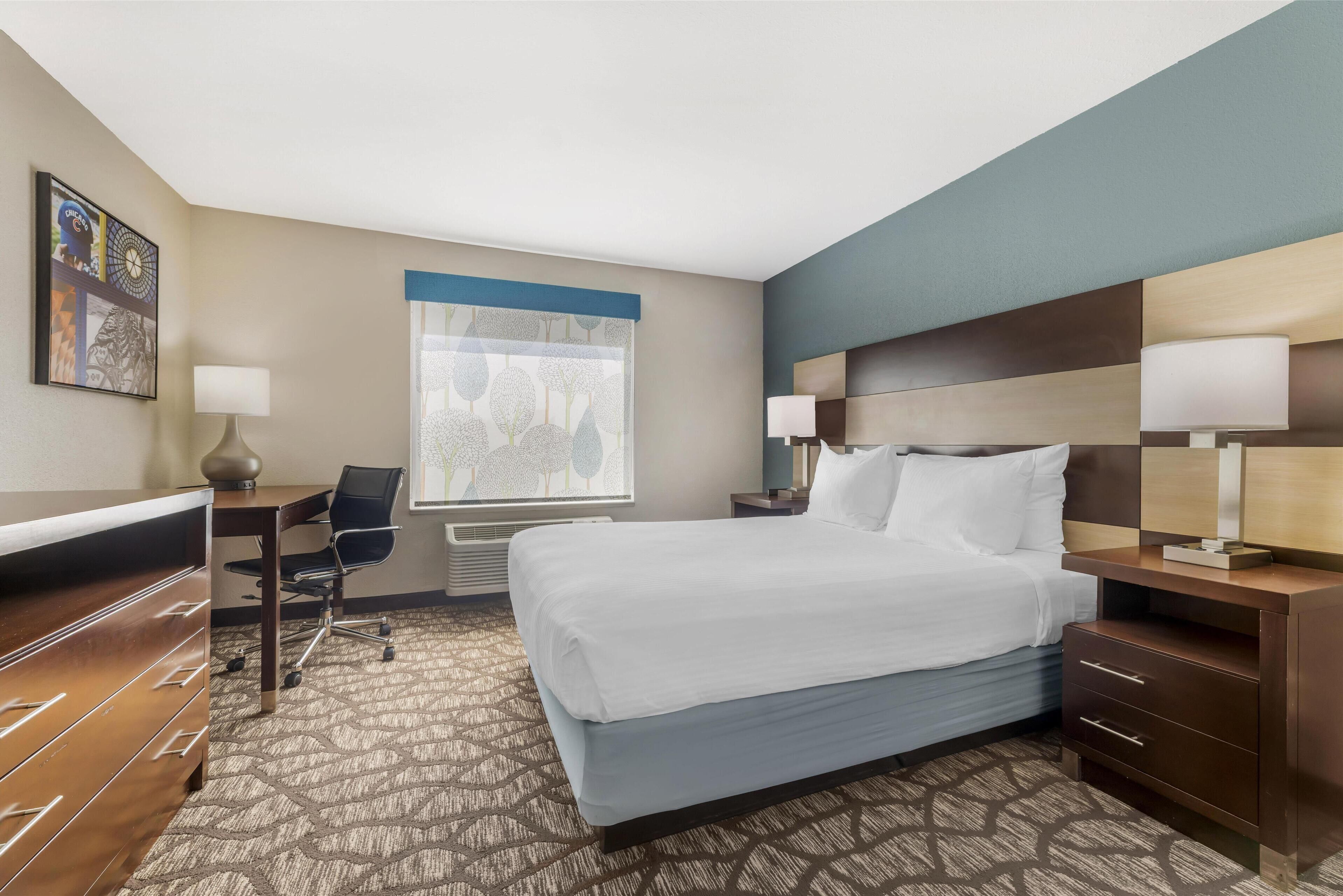 A hotel room with a bed, desk, chair, and dresser.