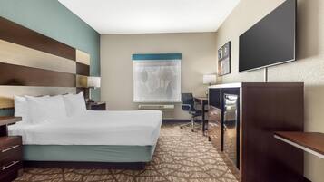 A hotel room with a large bed, a desk with a chair, a flat-screen TV, a wardrobe, and a window with a curtain.