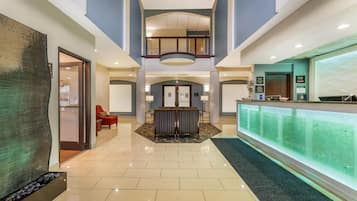 A hotel lobby with a reception desk, seating area, and a glass wall.