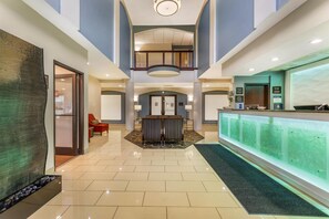Een hotellobby met een receptiebalie, een zithoek en een glazen wand.