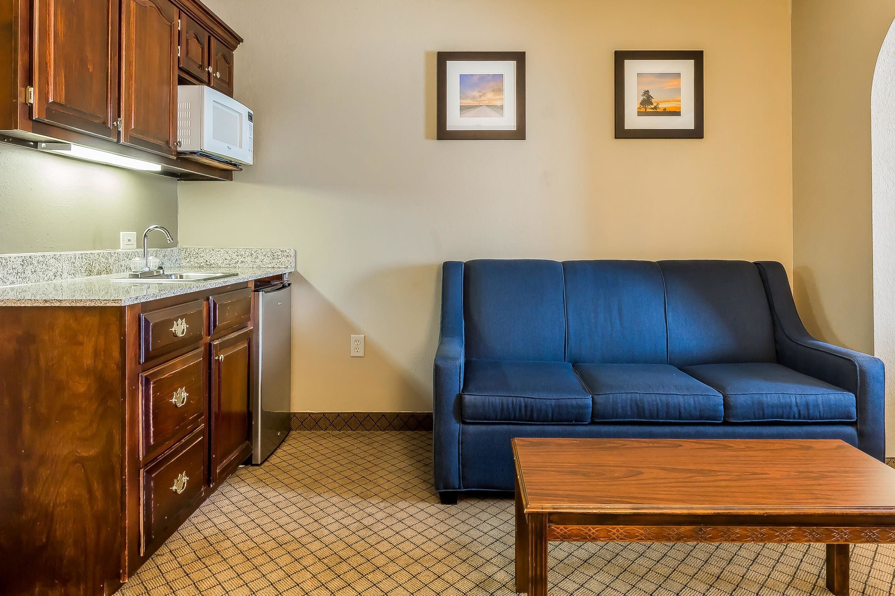A kitchen with wooden cabinets, a microwave, a sink, and a blue sofa. There are two framed pictures on the wall.