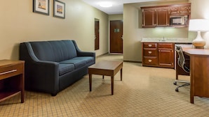 A living room with a sofa, a coffee table, a TV stand, and a kitchen area with cabinets and a microwave.