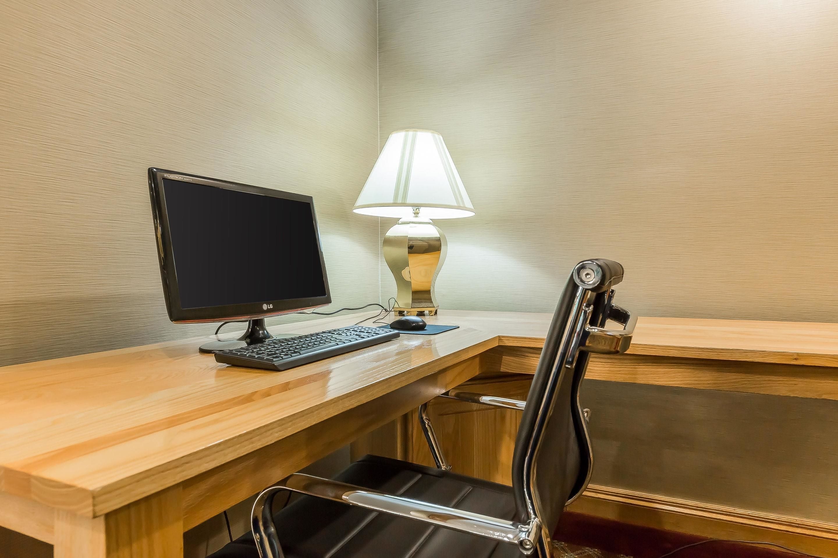 A wooden desk with a computer monitor, keyboard, and a lamp.