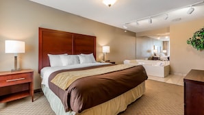 A hotel room with a large bed, bedside lamps, a wooden nightstand, a bathroom with a sink and mirror, and a potted plant.