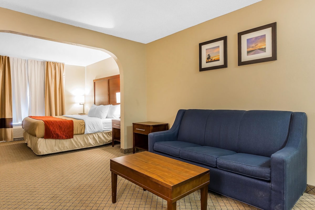 Een hotelkamer met een bed, een blauwe bank, een houten bijzettafeltje en twee ingelijste foto's aan de muur.