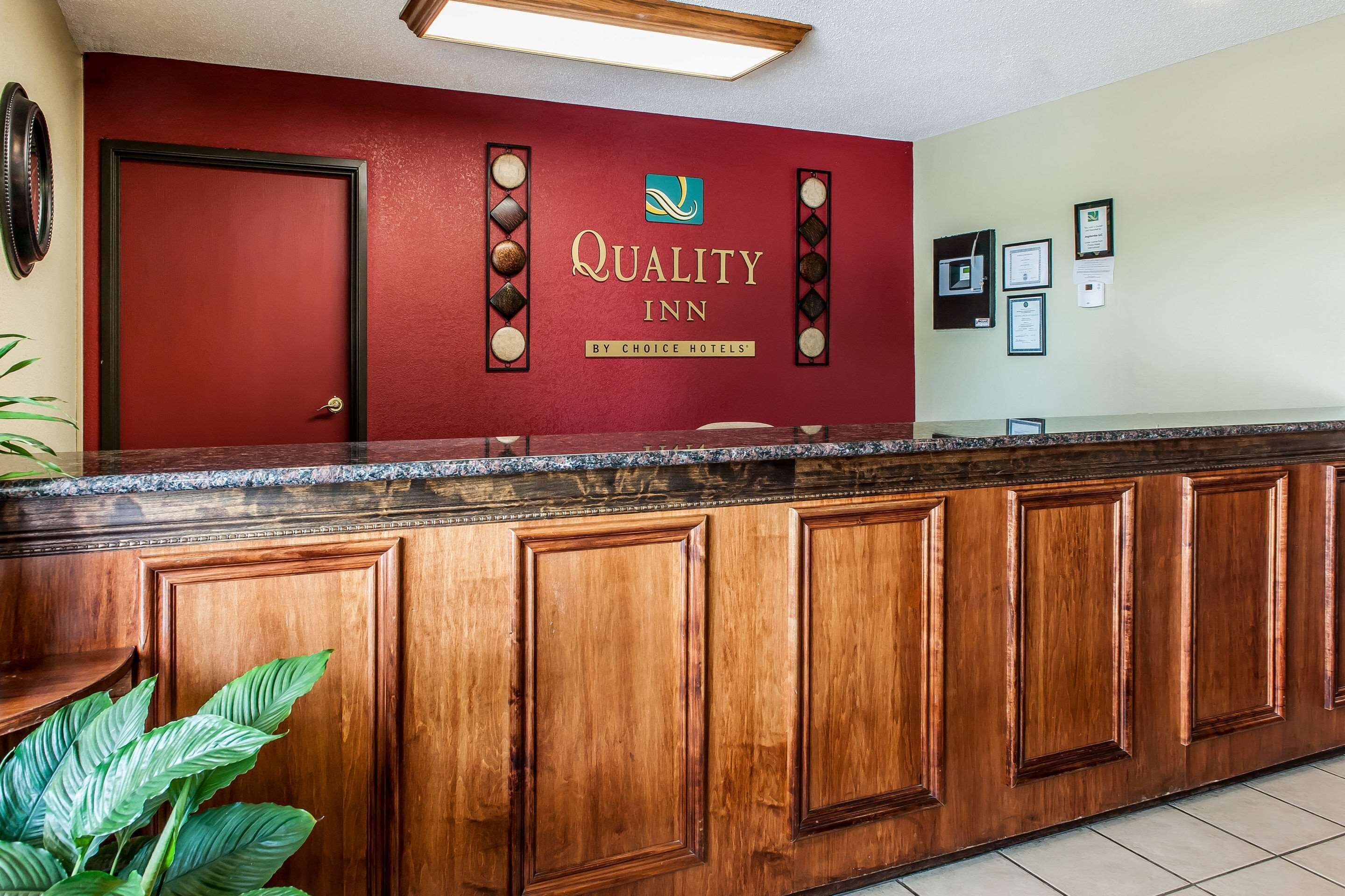 Un mostrador de recepción con una pared roja y el logotipo de Quality Inn by Choice Hotels.