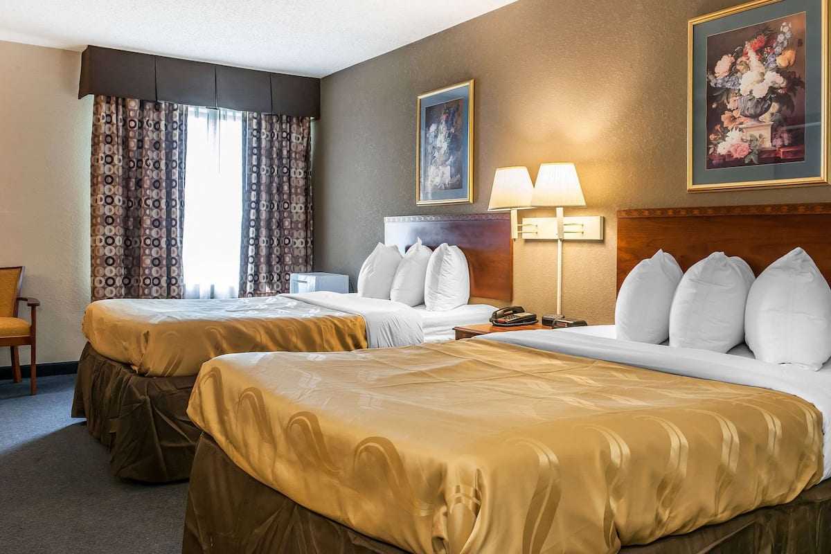 A hotel room with two beds, a headboard, a nightstand, a lamp, and a painting on the wall.