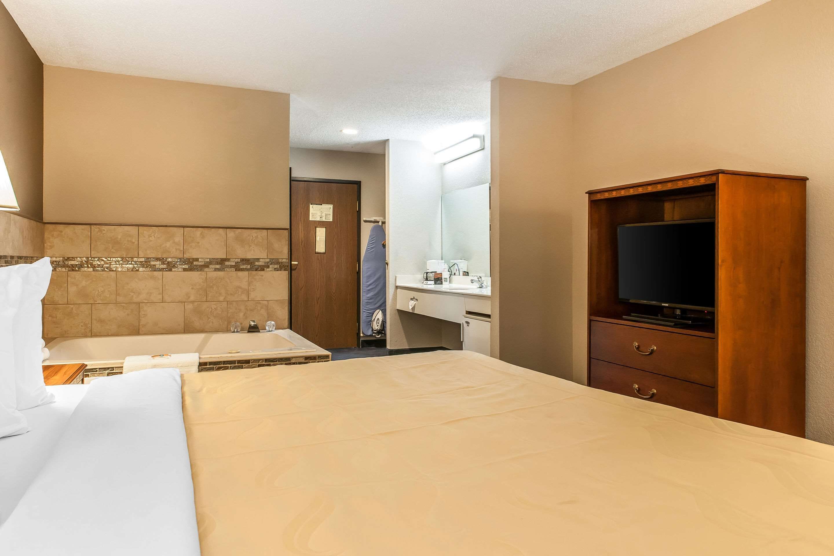 A hotel room with a bed, a TV, a desk, and a bathroom visible through an open door.