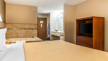 A hotel room with a bed, a TV, a desk, and a bathroom visible through an open door.