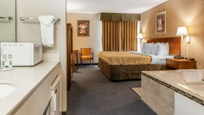 Ett hotellrum med en säng, ett skrivbord, en stol, en mikrovågsugn, ett handfat och ett badkar.