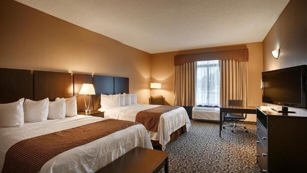 A hotel room with two beds, a desk, a chair, a television, and a window with curtains. - Inn at Coushatta (Kinder)