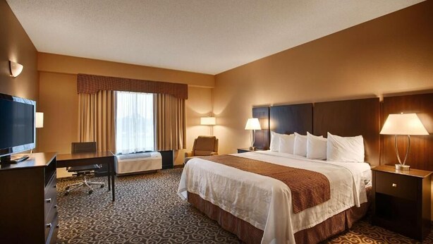 A hotel room with a large bed, a desk, a chair, a TV, and a window with curtains. - Inn at Coushatta (Kinder)