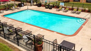 A rectangular swimming pool with a tiled deck, surrounded by a black metal fence. There are lounge chairs and a table with chairs along the poolside. - Inn at Coushatta (Kinder)