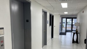 A clean, modern hallway with a black doormat, white tiled floors, and a door marked with a wheelchair symbol. - Americas Best Value Inn Donaldsonville (Donaldsonville)