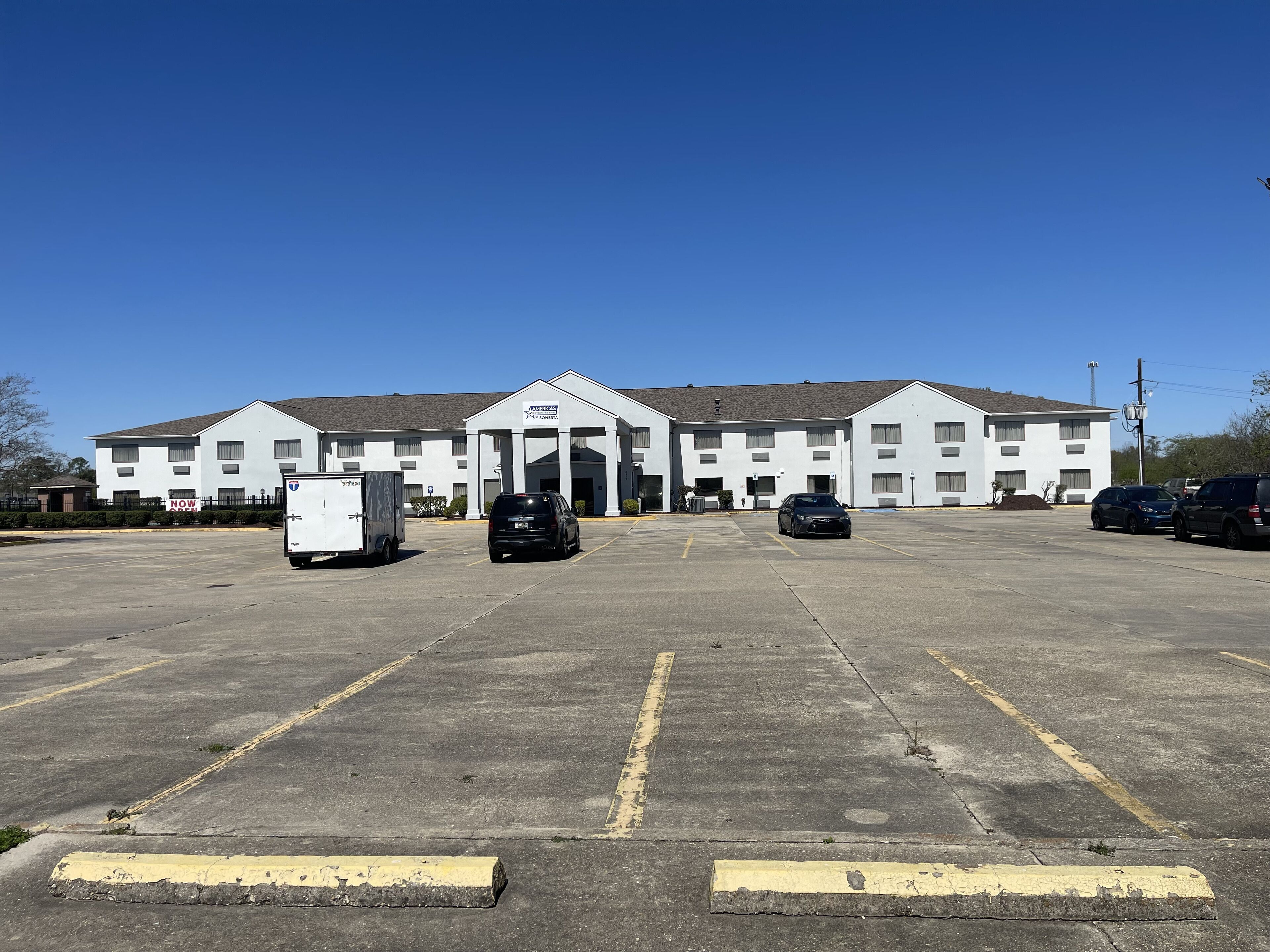 A large, white motel with a central entrance and multiple parking spaces.