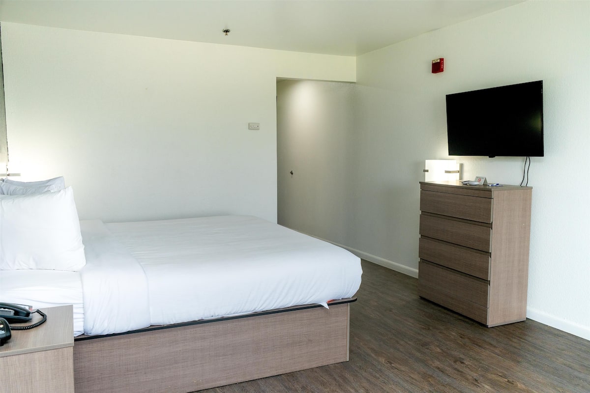 A hotel room with a bed, a dresser, a television, and a door leading to another room.