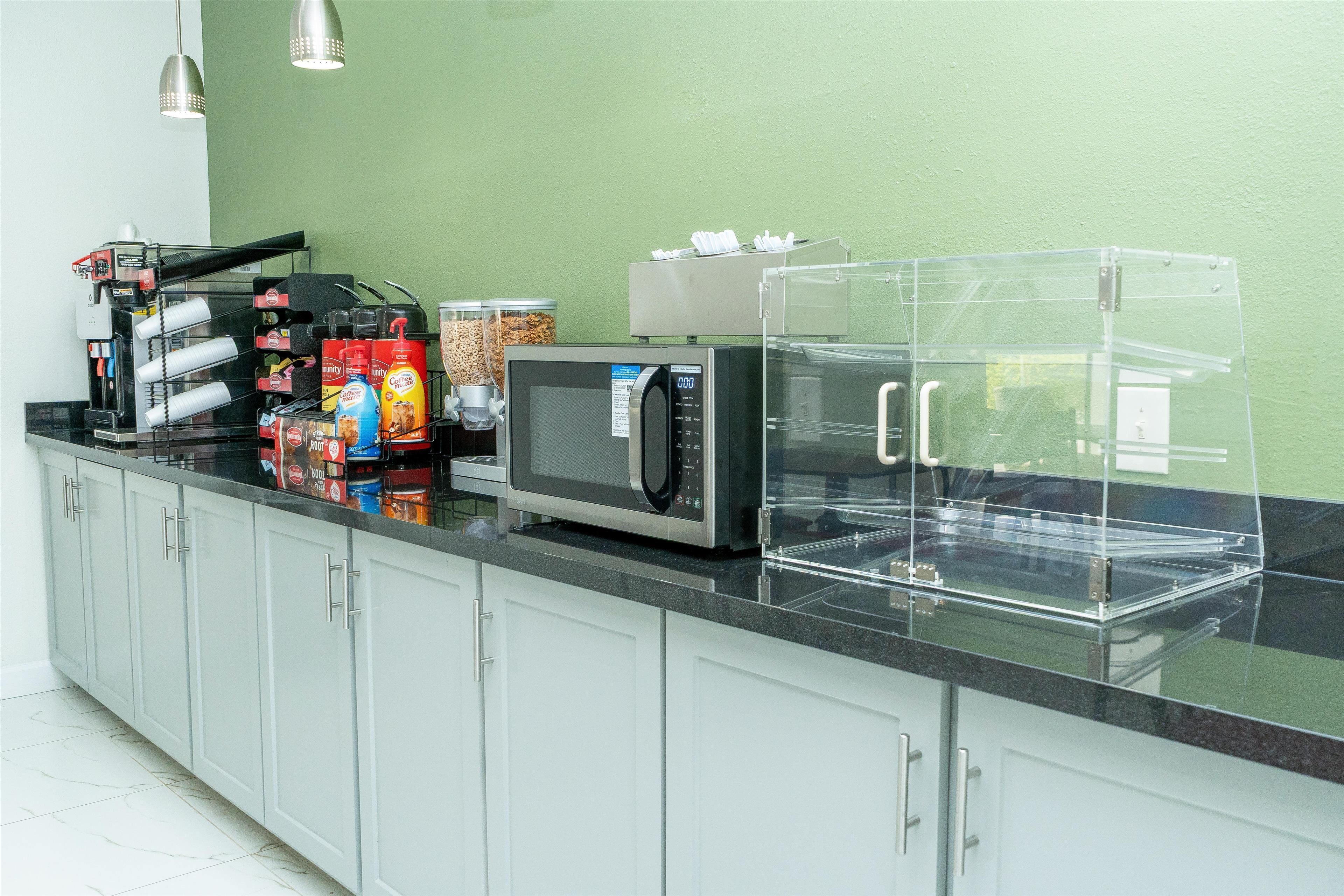 A kitchenette with a microwave, coffee machine, and various food containers.