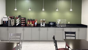 A kitchenette with a coffee machine, microwave, and various food items. There are cabinets, a table, and chairs. - Americas Best Value Inn Donaldsonville (Donaldsonville)
