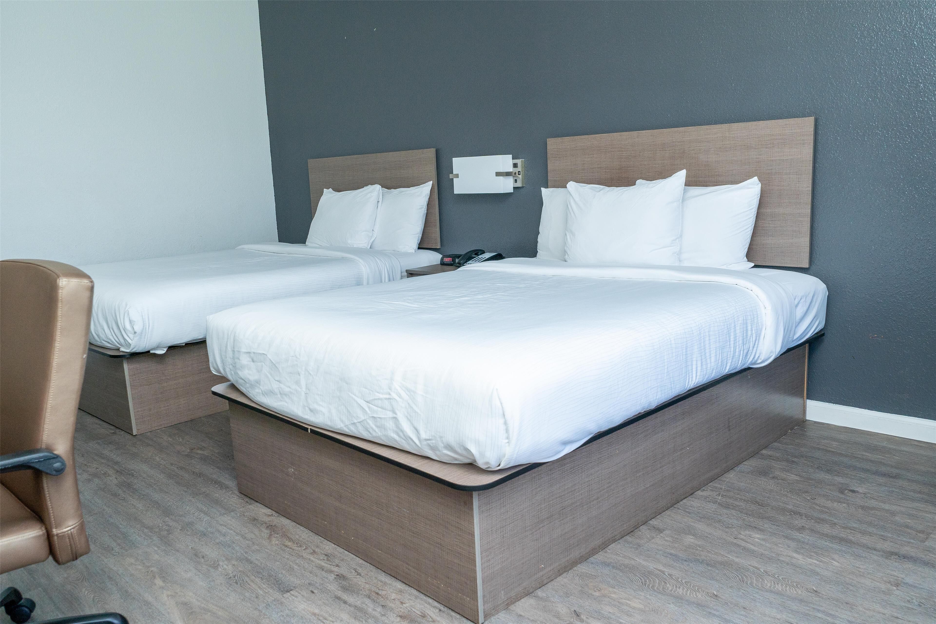 Ein Hotelzimmer mit zwei Einzelbetten, einem hölzernen Kopfteil, einem Nachttisch mit Lampe und einem braunen Ledersessel.