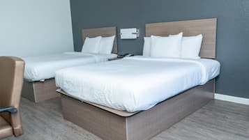 Ein Hotelzimmer mit zwei Einzelbetten, einem hölzernen Kopfteil, einem Nachttisch mit Lampe und einem braunen Ledersessel.