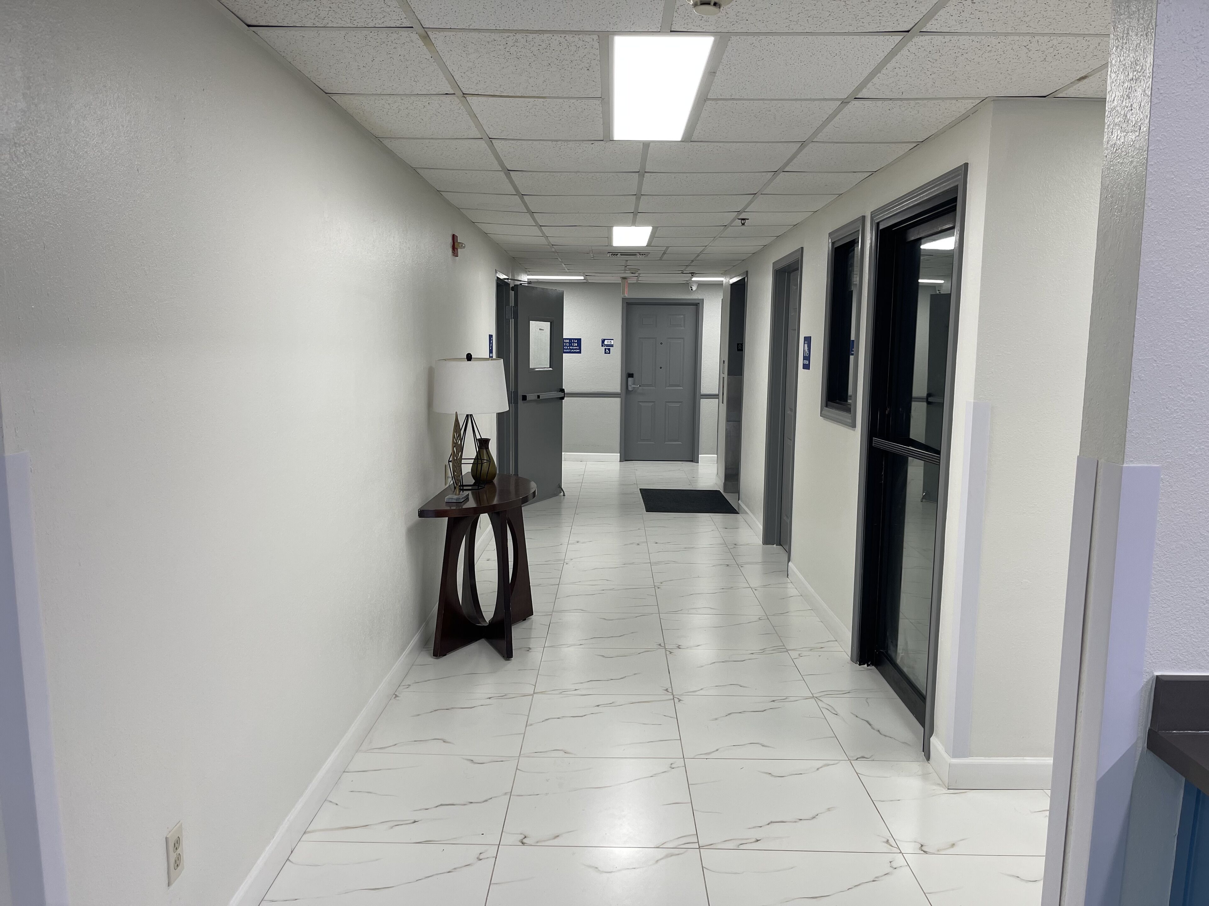 A clean, well-lit hallway with white walls and a tiled floor, leading to a reception area.