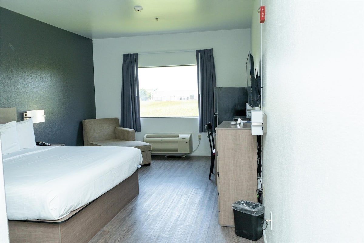 A hotel room with a bed, a desk, a chair, an air conditioner, and a window with curtains.
