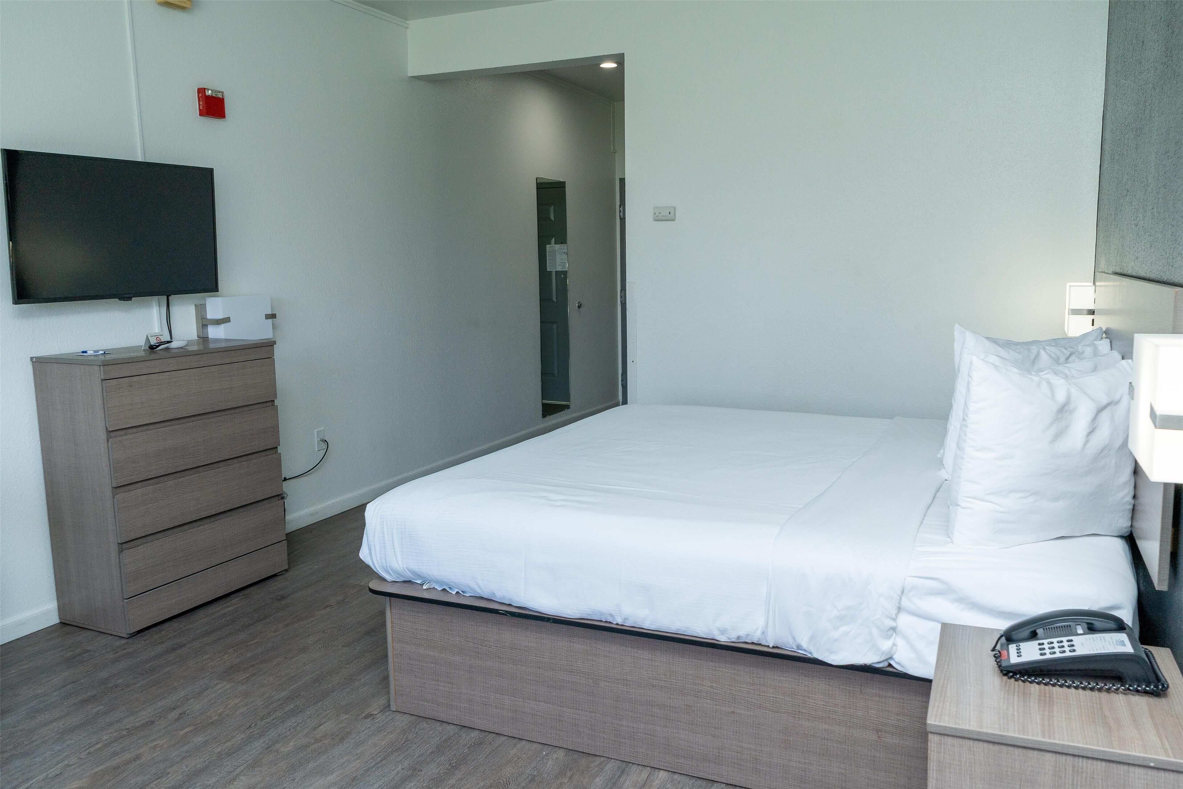 Une chambre d’hôtel avec un lit, une commode, une télévision et un téléphone sur la table de chevet.