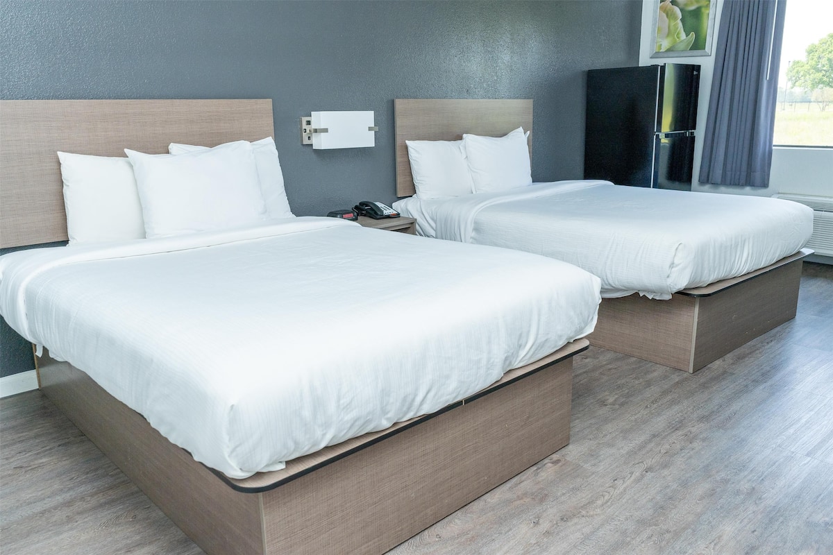 A hotel room with two beds, a nightstand, a phone, and a wall-mounted TV.