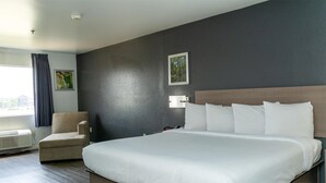 A hotel room with a large bed, a chair, a wall-mounted lamp, and a picture on the wall. - Americas Best Value Inn Donaldsonville (Donaldsonville)
