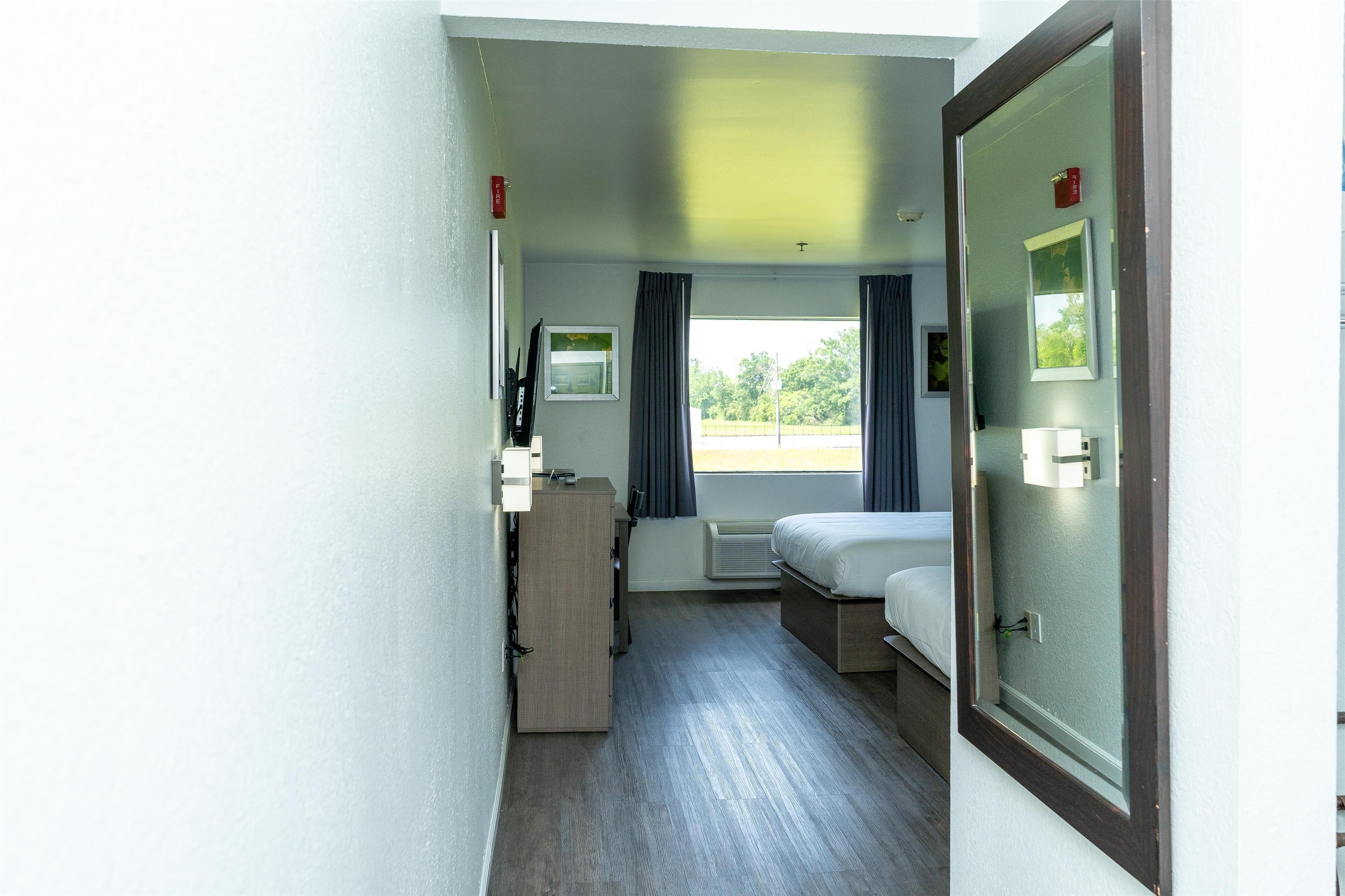 A narrow hotel room with a bed, a desk, and a window with curtains.
