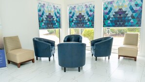 A waiting area with four chairs, a tiled floor, and large windows with geometric blinds. - Americas Best Value Inn Donaldsonville (Donaldsonville)