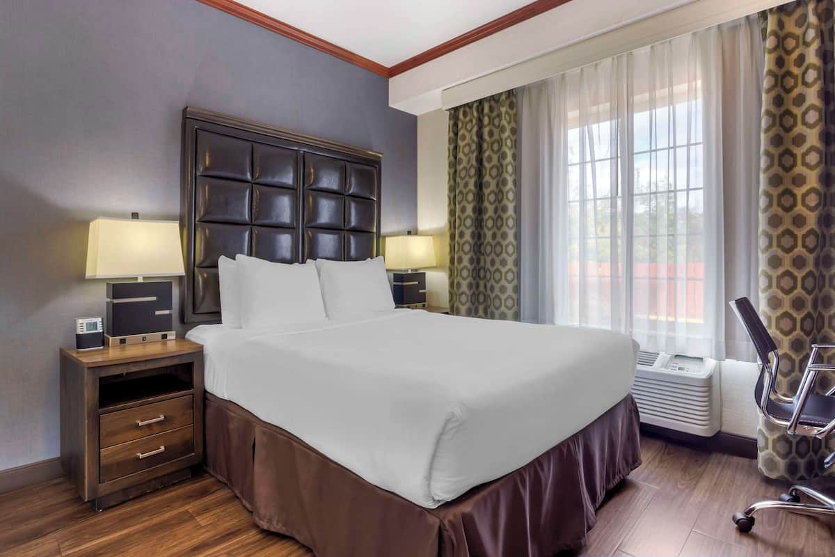 A hotel room with a large bed, two bedside tables with lamps, a chair, and a window with curtains.