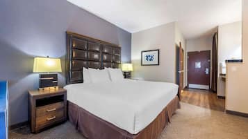 A hotel room with a large bed, a nightstand with a lamp, a dresser, and a door leading to another room.