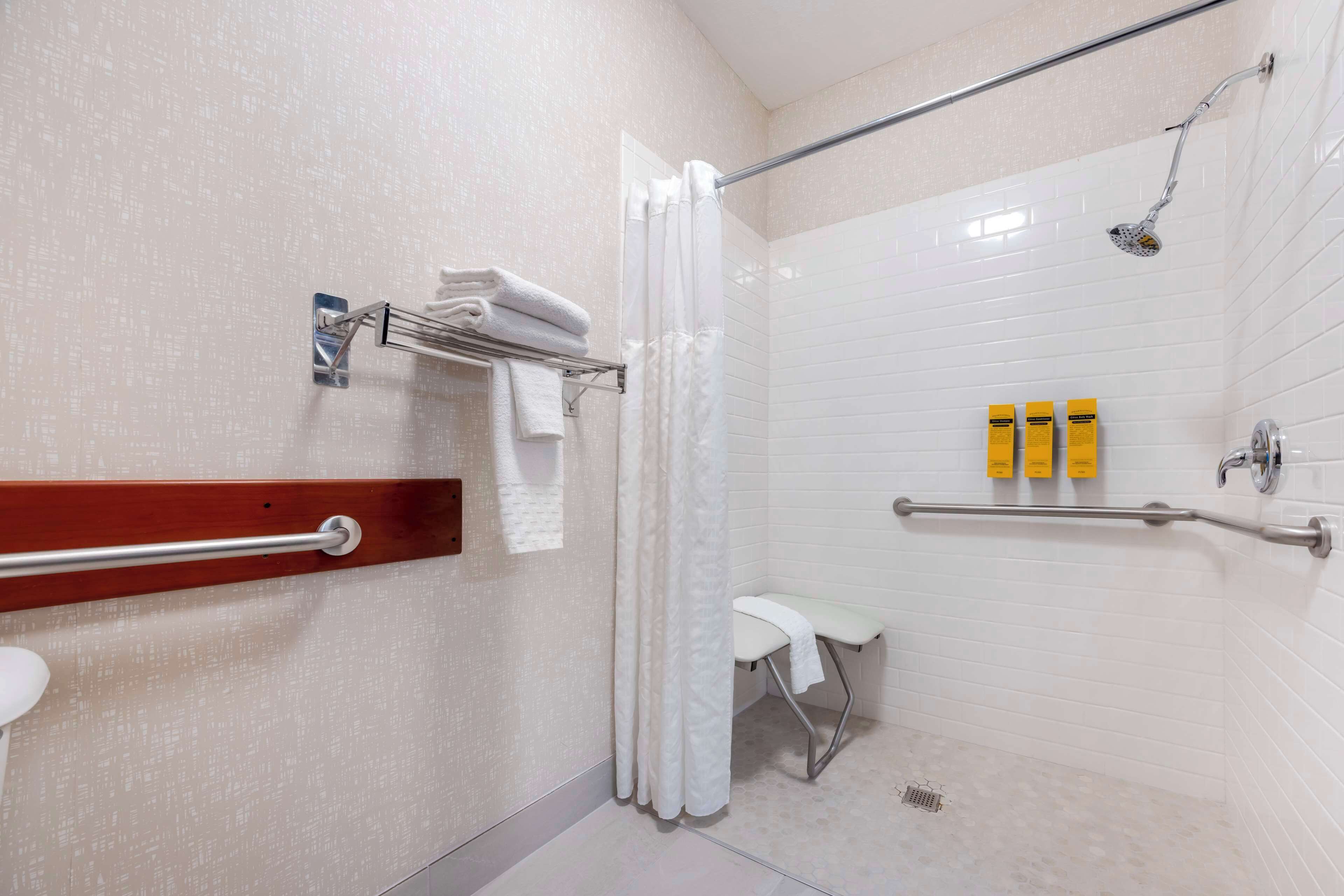 Une salle de bain moderne équipée d’une douche, d’une barre d’appui, d’un banc blanc et d’un porte-serviettes.