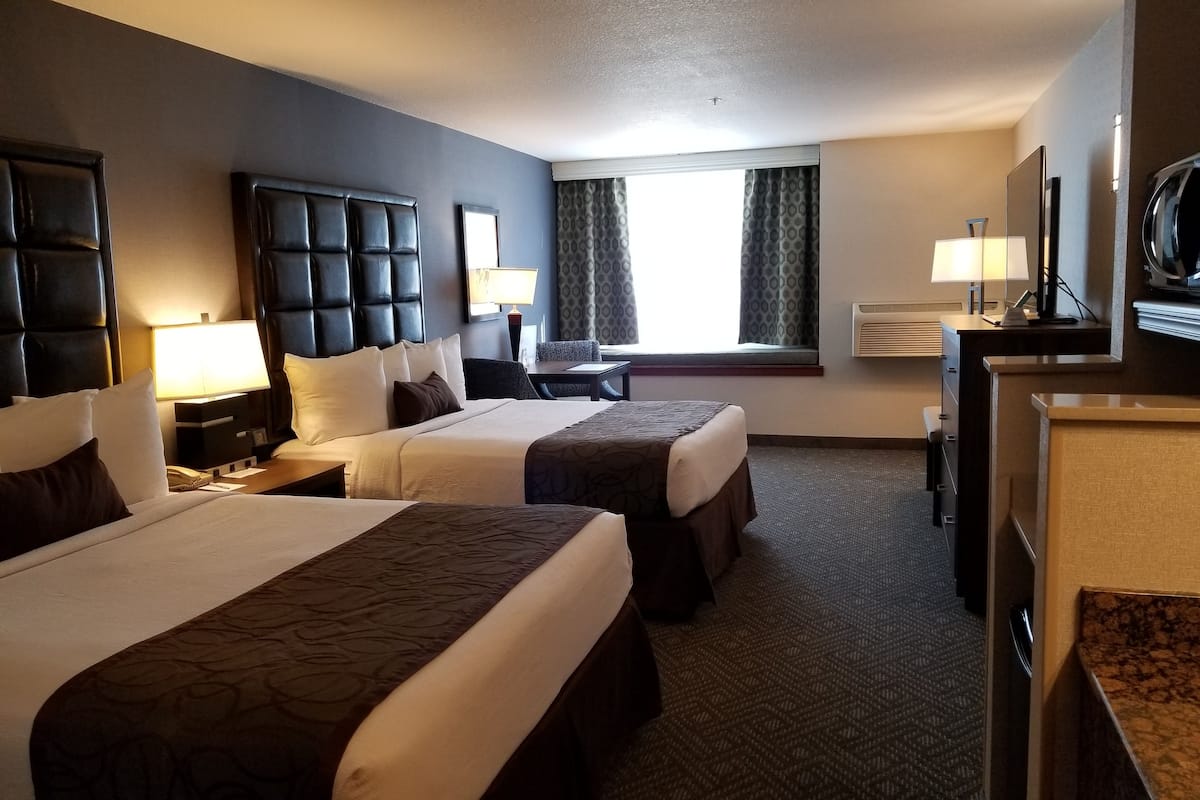 A hotel room with two beds, a desk, a chair, a TV, and a window with curtains.