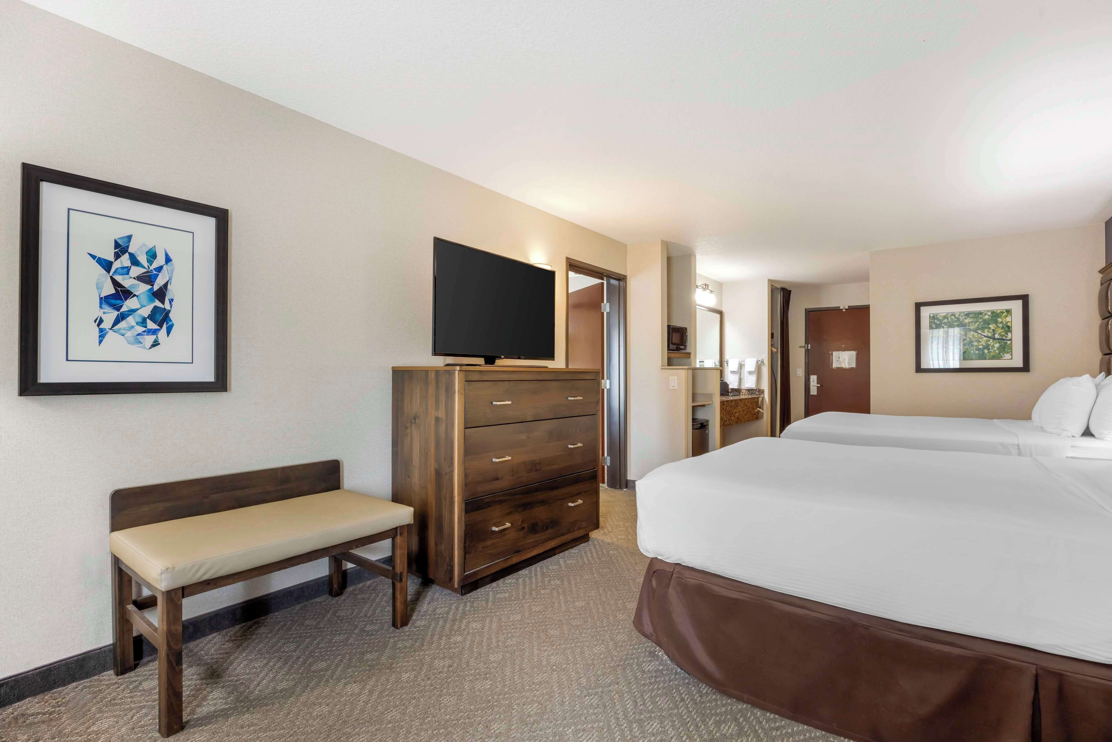 A hotel room with a bed, a bench, a dresser, a television, and artwork on the walls.