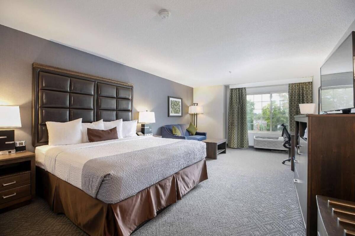 A hotel room with a large bed, bedside tables, a desk, a chair, and a television.