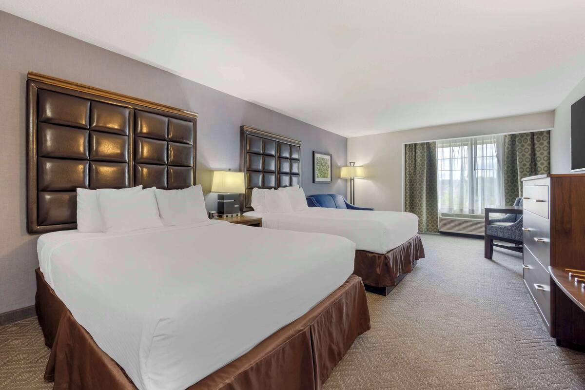 A hotel room with two beds, a desk, a chair, a dresser, and a large window with curtains.