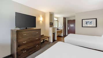 Habitación de hotel con televisión de pantalla plana sobre un tocador de madera, una cama, baño con espejo y un cuadro en la pared.