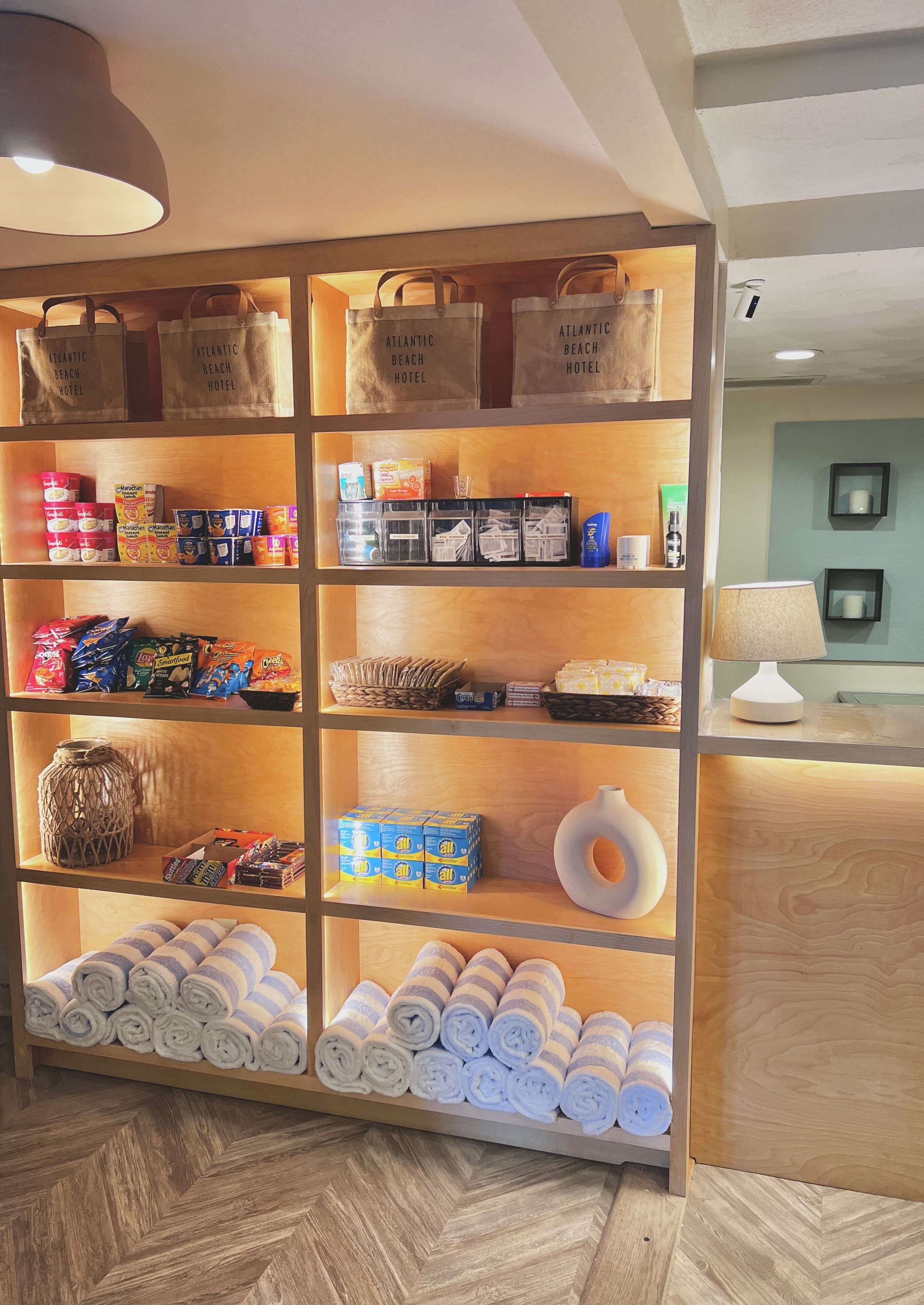 A hotel reception area with a wooden display shelf stocked with toiletries, snacks, and towels.