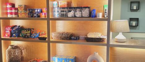 A hotel reception area with a wooden display shelf stocked with toiletries, snacks, and towels.