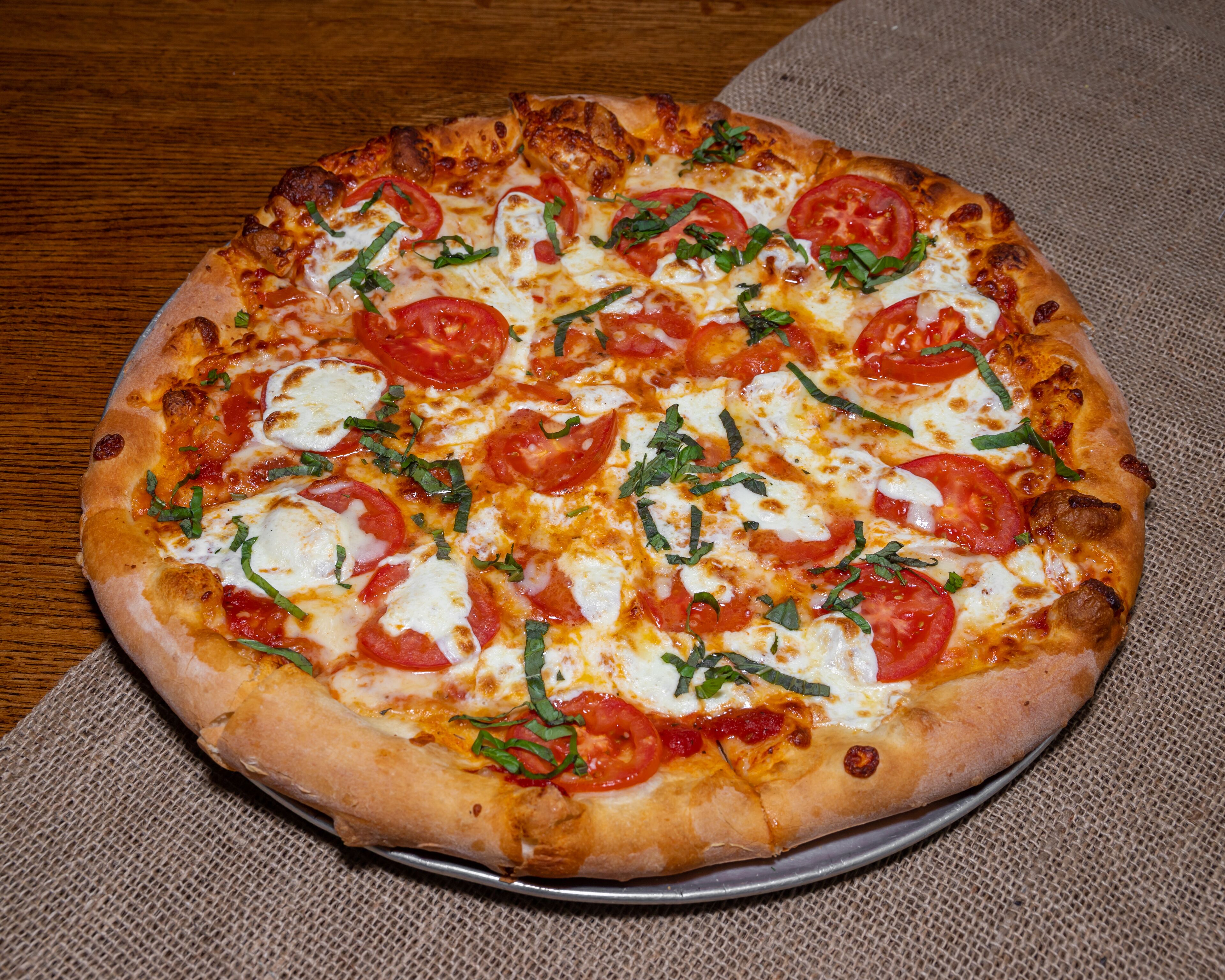 A pizza with tomato slices and cheese on a metal tray.