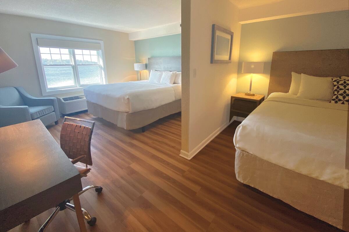 Een hotelkamer met twee bedden, een bureau en een stoel. Er is een raam met uitzicht op het water.