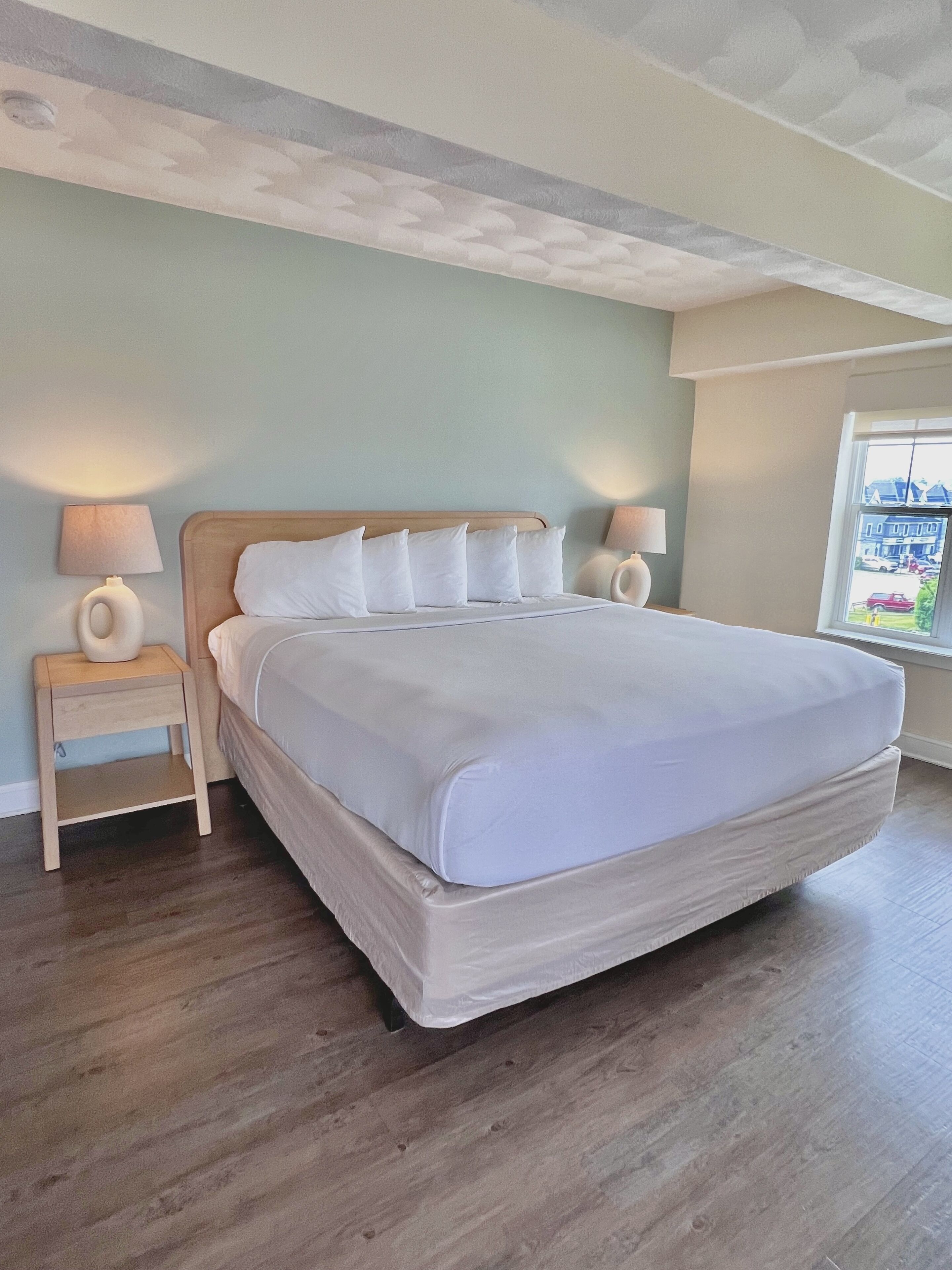 A bedroom with a large bed, two bedside tables, and a window with a view of the outside.