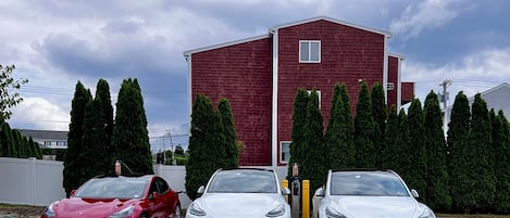Three cars parked in a lot with a red building and trees in the background.