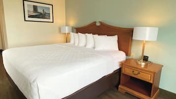 Una cama bien tendida con sábanas blancas y un cabecero de madera, flanqueada por dos lámparas de noche y una mesita de noche de madera con un cajón.