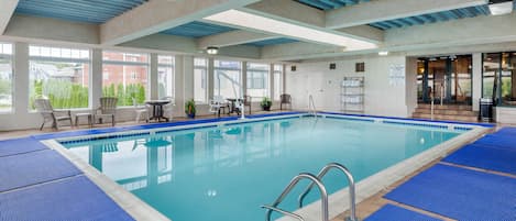 An indoor swimming pool with clear blue water, surrounded by blue mats, and a view of the outside through large windows.