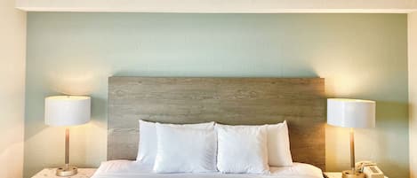 A neatly made bed with white linens and a wooden headboard, flanked by two bedside tables with lamps and a telephone.